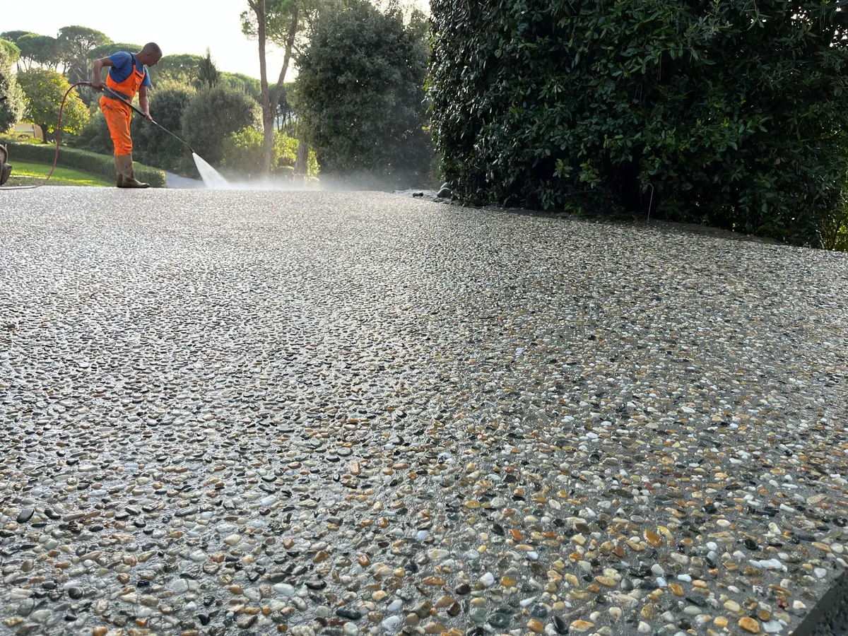 Operaio che lava una grande superficie in sasso lavato tra gli alberi