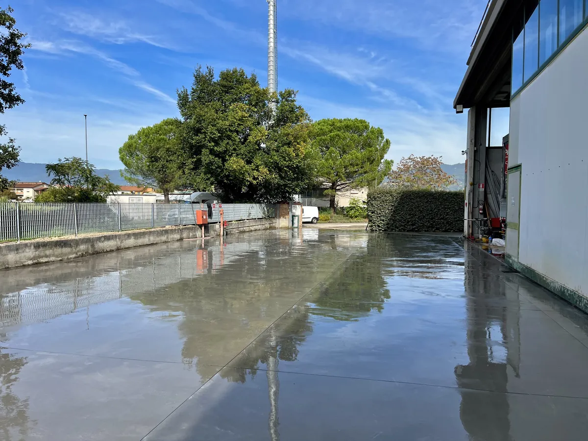 Piazzale industriale in calcestruzzo appena lisciato, bagnato e lucido, accanto a un capannone